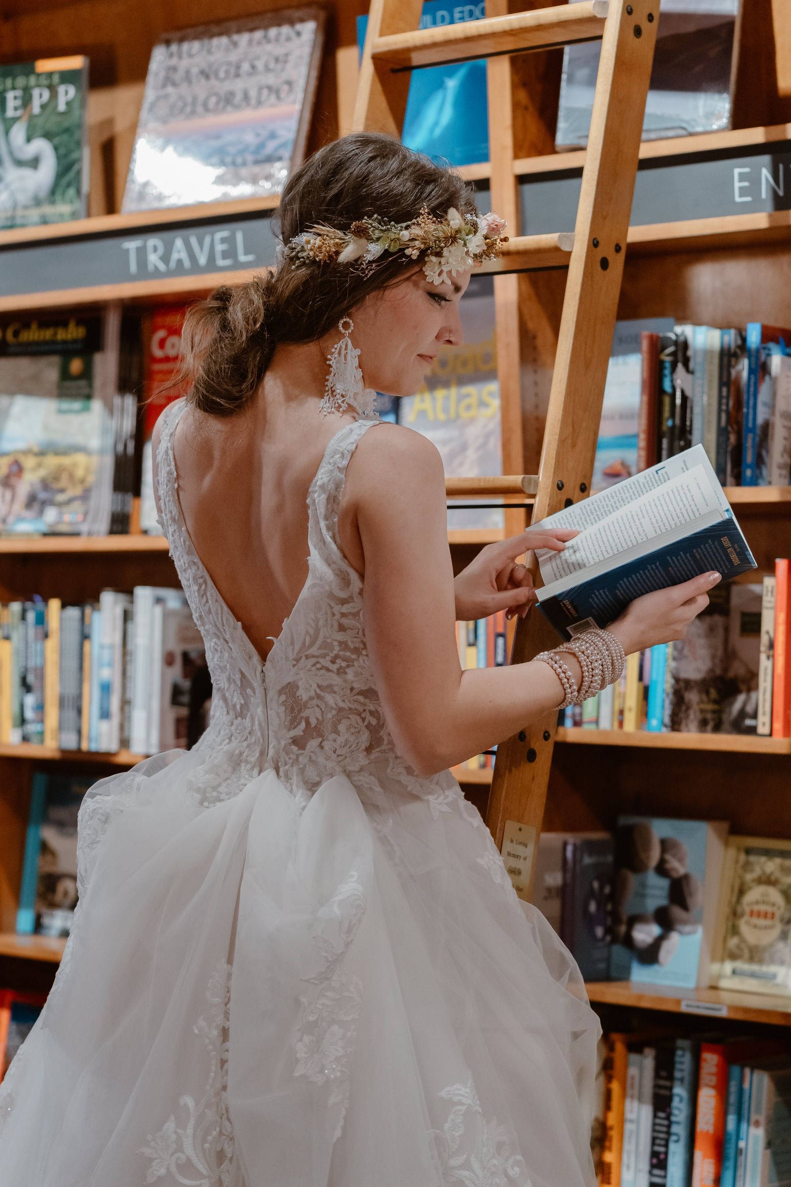 Leah wearing a flower crown and reading beside a wooden bookstore ladder